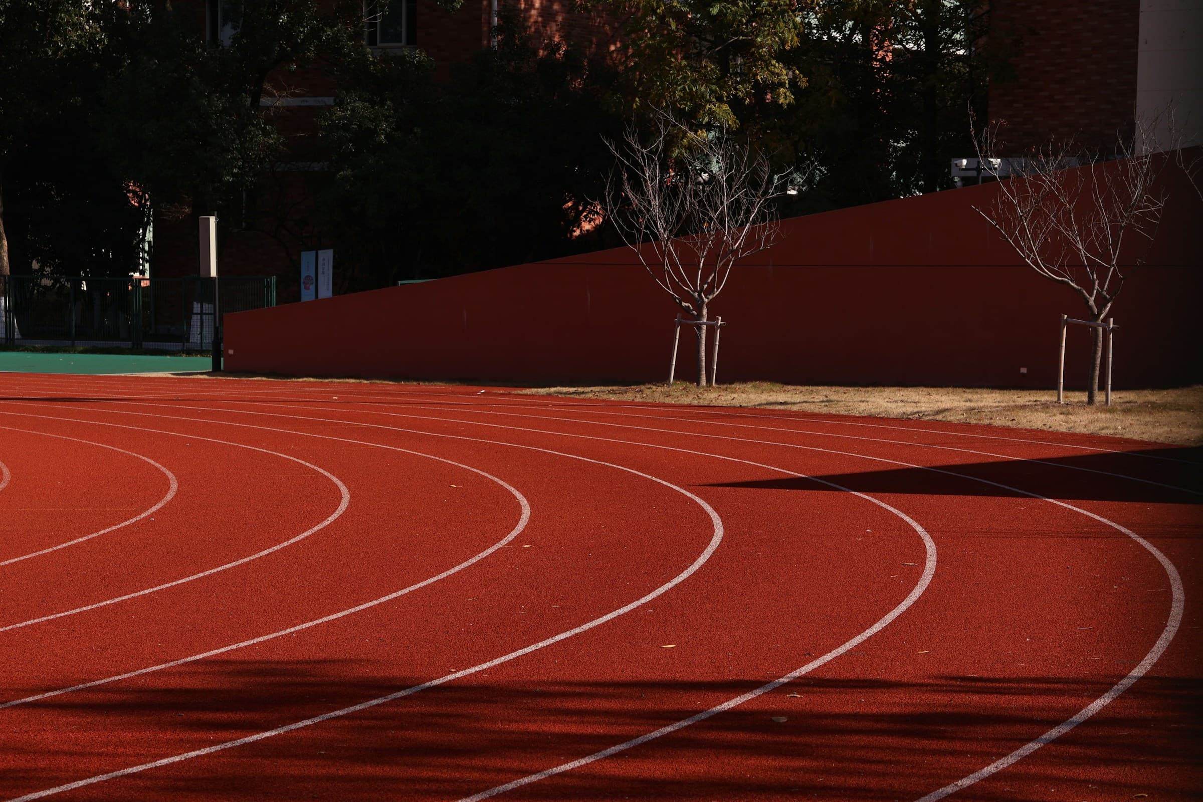 Curve van een rode atletiekpiste in middaglicht, regionale clubinfrastructuur